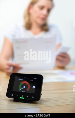 Frau Suchen an den inländischen Rechnungen mit Smart Energy Meter im Vordergrund Stockfoto