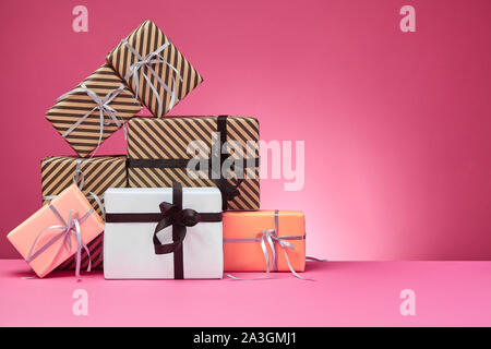 Verschiedene Größen, bunt gestreift und Normalpapier Geschenkboxen mit Bändern und Schleifen auf einem rosa Oberfläche und Hintergrund gebunden. Close-up, kopieren. Stockfoto