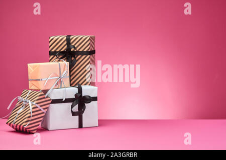 Verschiedene Größen, bunt gestreift und Normalpapier Geschenkboxen mit Bändern und Schleifen auf einem rosa Oberfläche und Hintergrund gebunden. Close-up, kopieren. Stockfoto