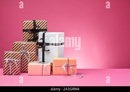 Verschiedene Größen, bunt gestreift und Normalpapier Geschenkboxen mit Bändern und Schleifen auf einem rosa Oberfläche und Hintergrund gebunden. Close-up, kopieren. Stockfoto