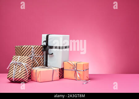 Verschiedene Größen, bunt gestreift und Normalpapier Geschenkboxen mit Bändern und Schleifen auf einem rosa Oberfläche und Hintergrund gebunden. Close-up, kopieren. Stockfoto