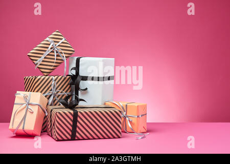 Verschiedene Größen, bunt gestreift und Normalpapier Geschenkboxen mit Bändern und Schleifen auf einem rosa Oberfläche und Hintergrund gebunden. Close-up, kopieren. Stockfoto