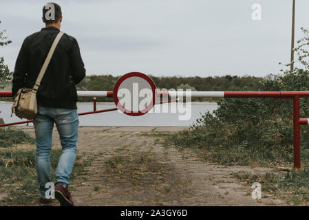 Mann, der in die Barriere mit einem kein Eintrag anmelden. Straße führt in den Fluss. Stockfoto