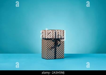 Gestreifte braune Papier-vorhanden-Box mit schwarzen Band und Bogen auf blauem Untergrund und Hintergrund gebunden. Close-up, kopieren. Stockfoto