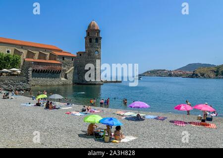 Frankreich, Pyrenees Orientales, Collioure, Urlauber unter den Sonnenschirmen auf boramar Strand mit Unserer Lieben Frau von den Engeln Kirche aus dem 17. Jahrhundert im Hintergrund Stockfoto