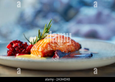 Nahaufnahme von Stück leckeren roten Lachs serviert mit Obst garniert auf Platte im Restaurant. Gesundes Gericht in Cafe auf unscharfen Hintergrund gekocht. Konzept der Diät, Meeresfrüchte und Protein. Stockfoto