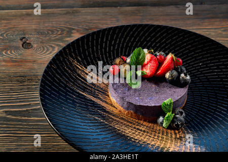 Ansicht von oben von leckeren Käsekuchen mit Heidelbeeren bleiben auf schwarze Platte auf dem Tisch. Leckeres Dessert mit Erdbeeren und frischer Minze und pulverisierte mit Kakao. Konzept der Nahrung. Stockfoto