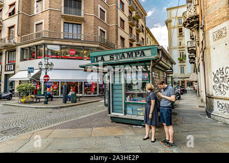 Ein paar steht neben einem grünen La Stampa Kiosk, während der Mann auf sein Handy auf der Via Pietro Micca, Turin Italien sieht. Stockfoto