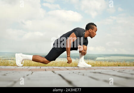 Leichtathlet Übungen mit Stretching für die Füße am Morgen. Stattliche Sportsman posiert im Freien. Mann mit sportlicher Körper tragen in weißen Socken und Turnschuhe. Stockfoto