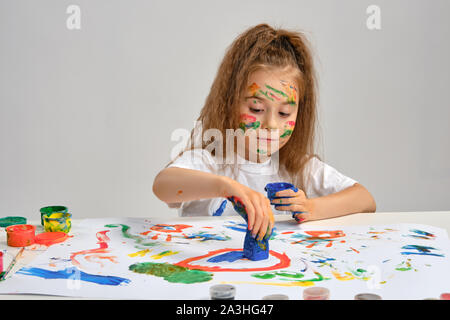 Kleines Mädchen im weißen T-Shirt mit whatman und Farben sitzen, Zeichnung, mit bemaltem Gesicht, Hände. Auf weiß isoliert. Close-up. Stockfoto