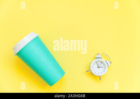 Einfach flach Design blaues Papier Kaffeetasse und Wecker auf Gelb bunte trendy Hintergrund isoliert. Takeaway trinken Frühstück trinken. Guten Morgen aufwachen wach Konzept. Ansicht von oben kopieren Raum Stockfoto