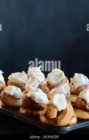 Frische hausgemachte groß Zimt Brötchen mit Frischkäse noch Vereisung in der Muffin tin. Selektiver Fokus auf zweiten Bun in Zentrum mit verschwommenen Hintergrund. Stockfoto