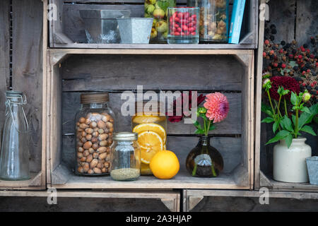 Altmodische, mit Früchten und Nüssen infundierte Gin-Gläser mit Vasen aus geschnittenen Blumen in einer Holzkiste. VEREINIGTES KÖNIGREICH Stockfoto