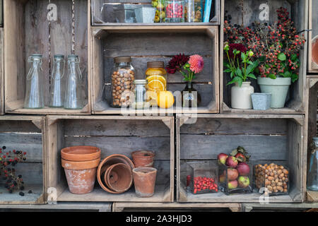 Altmodische, mit Früchten und Nüssen infundierte Gin-Gläser mit Vasen aus geschnittenen Blumen in einer Holzkiste, Großbritannien Stockfoto