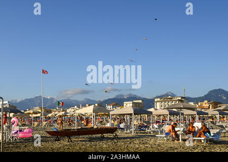 Blick auf den Sandstrand von Lido di Camaiore, beliebtes Reiseziel an der Versilia Küste, mit Touristen, fliegende Drachen und Raw-Boot, Toskana, Italien Stockfoto