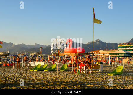 Malerischer Blick auf den Sandstrand von Lido di Camaiore mit einem rosa Aufblasbare Flamingo, moderne Strand Liegestühle und einen Panoramablick auf das Rad, Toskana, Italien Stockfoto