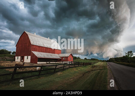 Dramatische Sturm Wolken ziehen über einen roten Scheune auf einer Landstraße. Stockfoto