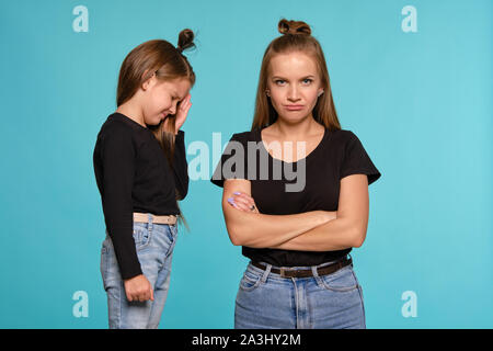 Mutter und Tochter mit einem lustigen Frisuren, in schwarzen T-Shirts und blaue Jeans gekleidet posiert vor einem blauen studio Hintergrund. Nahaufnahme. Stockfoto