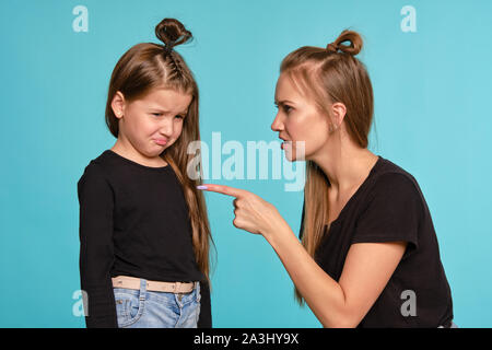 Mutter und Tochter mit einem lustigen Frisuren, in schwarzen T-Shirts und blaue Jeans gekleidet posiert vor einem blauen studio Hintergrund. Nahaufnahme. Stockfoto