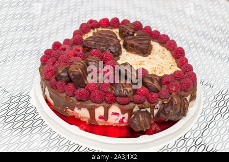 Vegan herzförmige Schokolade Kuchen gekrönt mit Himbeeren auf weißen Küche Hintergrund. Top Winkel betrachten. Stockfoto