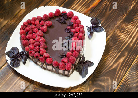 Veganer Käsekuchen für Liebhaber mit Himbeeren auf weiße Platte mit Basilikum. Ansicht von oben. In der Form von Herzen gekocht. Stockfoto