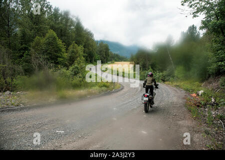 Eine Frau reitet ihr Motorrad auf einer Schotterstraße in Kanada. Stockfoto