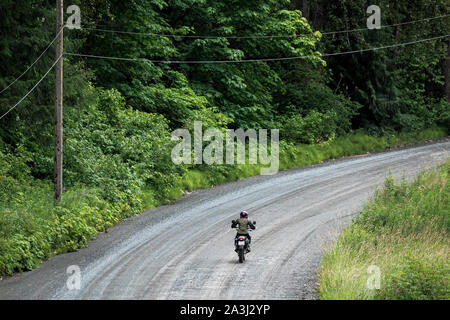 Eine Frau reitet ihr Motorrad auf einer Schotterstraße in Kanada. Stockfoto