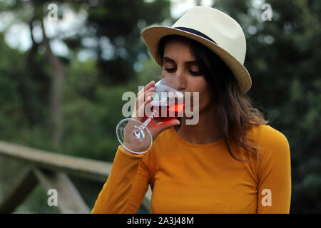 Junge Mädchen in Gelb und in einen Hut trinkt ein Glas Rose Wein gekleidet. Picknick- und Freizeitaktivitäten im Freien. Stockfoto