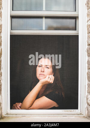 Frau Suchen aus offenen Fenster mit Kinn auf der Hand. Stockfoto