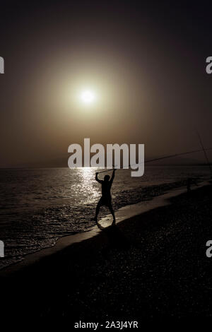 Silhouette der Fischer am Strand mit Fisch Stange stehend auf Meerwasser Fischen bei Sonnenuntergang mit einer wunderschönen Golden Sky in Ferien Hobby- und Lei entspannen Stockfoto