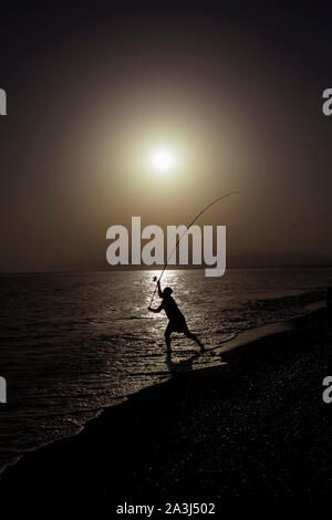 Silhouette der Fischer am Strand mit Fisch Stange stehend auf Meerwasser Fischen bei Sonnenuntergang mit einer wunderschönen Golden Sky in Ferien Hobby- und Lei entspannen Stockfoto
