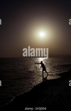 Silhouette der Fischer am Strand mit Fisch Stange stehend auf Meerwasser Fischen bei Sonnenuntergang mit einer wunderschönen Golden Sky in Ferien Hobby- und Lei entspannen Stockfoto