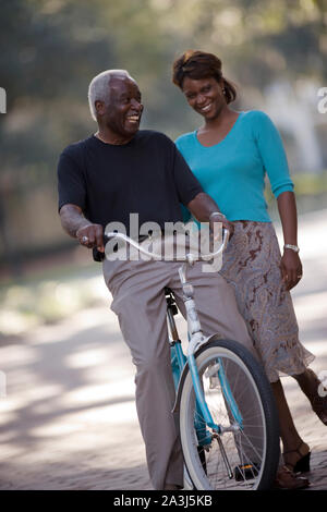 Lächelnd älterer Mann sitzt auf einem Fahrrad neben seiner Mitte erwachsenen Tochter. Stockfoto