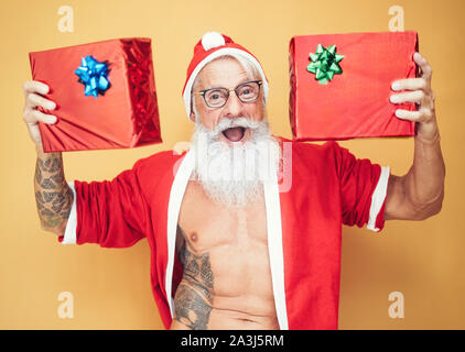 Tätowiert passen santa claus Holding Weihnachten Geschenke - trendige Bärtigen hipster Senior tragen xmas Kleidung Übersicht präsentiert Stockfoto