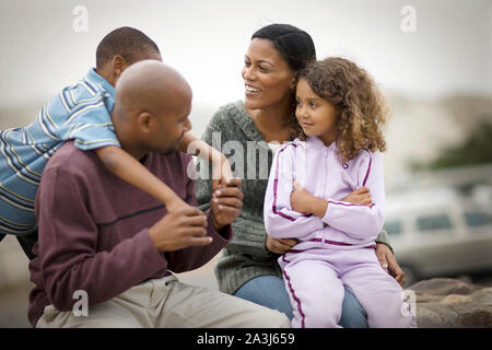 Gerne Mitte - erwachsene Paare und ihre zwei kleinen Kinder sitzen auf einer Mauer aus Stein im Freien. Stockfoto