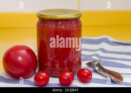 Vitamine auf gelbe Tabelle, Tomate, Kirsche und Tomatenmark in Glas und Dosenöffner auf gestreiftes Handtuch Stockfoto