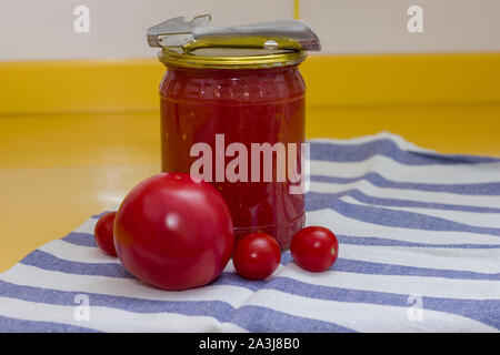 Vitamine auf gelbe Tabelle, Tomate, Kirsche und Tomatenmark in Glas und Dosenöffner auf gestreiftes Handtuch Stockfoto