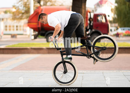 Ein junger Kerl auf einem BMX Bike, Fahrten auf dem Vorderrad, Bremsen mit seinem Fuß. Stockfoto