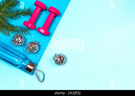 Weihnachten Sport mit rosa Hanteln, eine Flasche Wasser, einen Tannenbaum Zweige auf Blau Yogamatte und disco Kugeln Dekoration auf Pastell blau hinterlegt. Fla Stockfoto