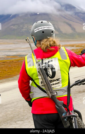 Frau auf Fahrrad trägt Eisbär Gewehr, Longyearbyen, Svalbard, Norwegen Stockfoto