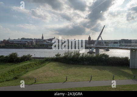 Der Peace Bridge über den River Foyle mit Derry/Londonderry Skyline im Hintergrund Stockfoto