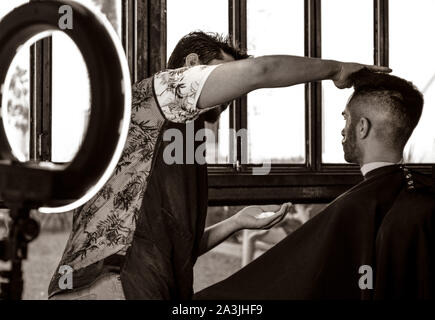 Nachdem ein neuer Haarschnitt, Friseur preps einen Client für ein mit Hilfe eines modernen Ringlicht bei '81 Friseure im Tucson, AZ, USA rasieren Stockfoto