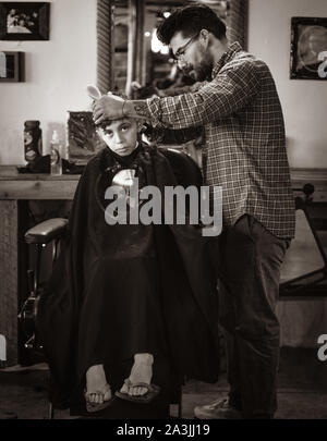 Trendy, stattlich, tausendjährigen Friseur, erstellt eine Hip Haarschnitt für eine Big eyed Boy bei '81 Friseure im Tucson, AZ, USA Stockfoto