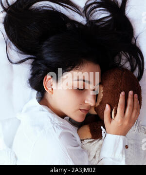 Junge Frau schlafen mit einem Spielzeug tragen. Schwarzhaarige Frau im Bett ruht mit Wohlgefallen niedlich. Einsame Frau im Bett mit einem Bären Spielzeug. Das glückliche Leben in eine einzige Dame Stockfoto