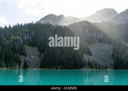 Die Sonne scheint durch Regen und Wolken über Joffre Lake. Stockfoto