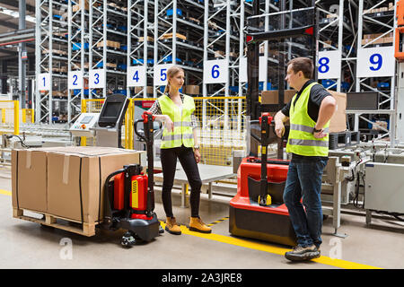 Lagerhaus Mitarbeiter in Uniform in der Nähe von Hubwagen und Gabelstapler in modernen automatischen Lager. Die Kisten sind in den Regalen des Lagerhauses Stockfoto