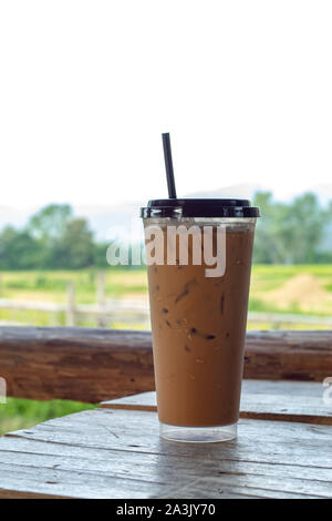 Eiskaffee auf dem Holzboden hinter einem Reisfeld. Stockfoto