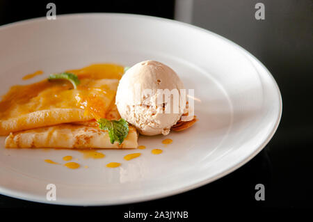 Französische Crêpe mit frischen Sweet Orange Sauce gebackene Mandel- und Vanilleeis in Weiß auf Schwarz Tabelle Stockfoto