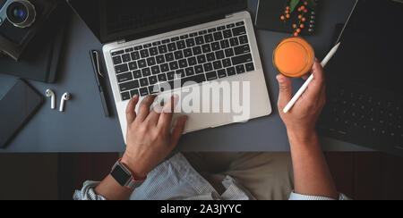 Blick von oben auf die Menschen mit der Arbeit an seinem Projekt mit Laptop beim Trinken ein Glas Orangensaft in dunklen modernen Arbeitsbereich Stockfoto
