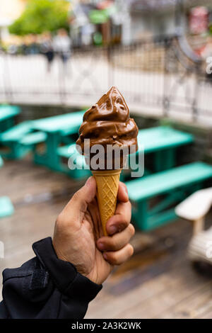 Mann mit Abblendlicht Schokolade Eis in der Hand, sehr unscharfen Hintergrund, kleine Tiefenschärfe. Der dunkle Hintergrund. Stockfoto